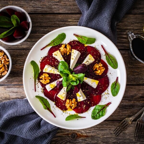 ote-Bete-Carpaccio mit Ziegenkäse, karamellisierten Walnüssen und Balsamico-Dressing auf einem weißen Teller